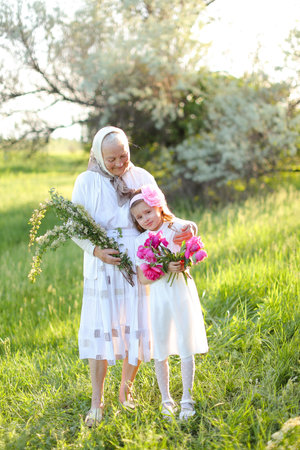 Old grandmother standing with little granddaughter and keeping flowers.の写真素材