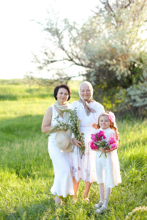 Caucasian old grandmother in white dress with daughter and granddaughter outside.の写真素材