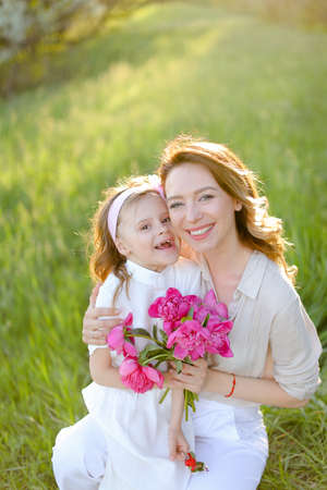 Portrait of happy young mother sitting with little daughter on grass.の写真素材