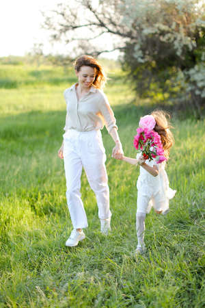 Young blonde mother walking with little daughter in grass.の写真素材
