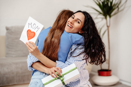 Happy mother's day. Child daughter congratulates mom and gives her postcard. Mum and girl smiling and hugging. Family holiday and togetherness. Mom is happy to receive an unexpected gift from her child.の写真素材