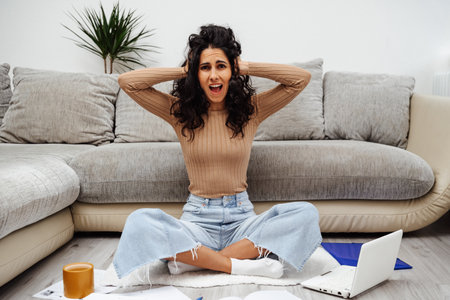 Young beautiful woman of Arab appearance holding her head in shock. Lots of paperwork at home and bad internet creates problems.の写真素材