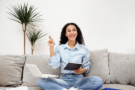 good idea. Beautiful young Arab woman appearance writes a wish list. Girl makes plans and schedules tasks while sitting on a gray sofa in home office.の写真素材