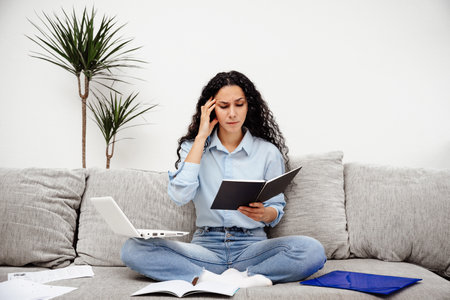 Beautiful young woman of Arabic appearance and thoughtful and trying to solve a problem in learning. Stressed girl holding her head from a lot of tasksの写真素材