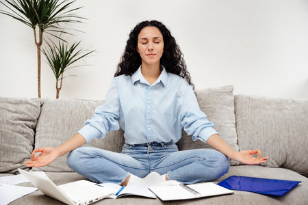 Beautiful young woman mixed race close your eyes and rest during work break. Relax sitting on sofa in yoga poseの写真素材