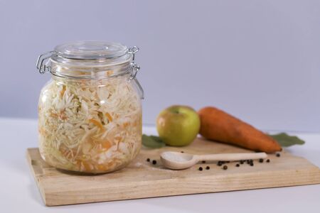 sauerkraut in a glass jar on wooden table. with carrots and mustard, sunflower oil, bay leaf and peas, on a gray background.Preserved vegetables. Top view, flat lay. Fermented food provides bacteria for a healthy digestive system. Preserved vegetables, healthy vegetarian, vegan food concept.の写真素材