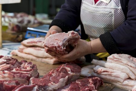 Piece of raw meat in the hands of the seller at the grocery market. High protein products for cooking meat dishes on the grill or in the oven. meat on the boneの写真素材