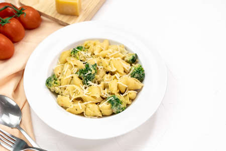 Pasta with green vegetables, broccoli, melted cheese and creamy sauce in white bowl on white table. Top view. Copy space.の写真素材
