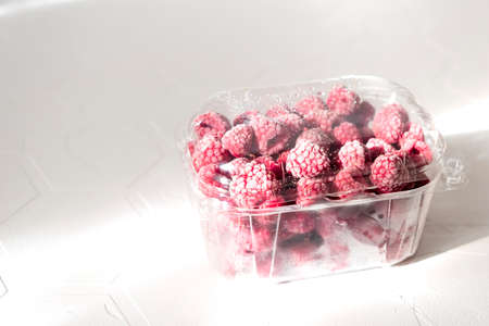 Plastic bag with frozen raspberry on white background with shadows, top view.の写真素材