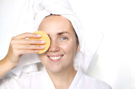 Spa and beauty concept. Happy young woman wearing white bathrobes towels on head doing spa procedures applying creme on her face in spa beauty salonの写真素材