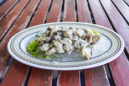 Fresh oysters The shell is laid on an ice pack in a white plate on a brown wood.の写真素材