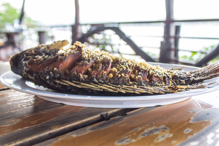 Tilapia fried in golden garlic, placed in a white plate on an old wooden table.