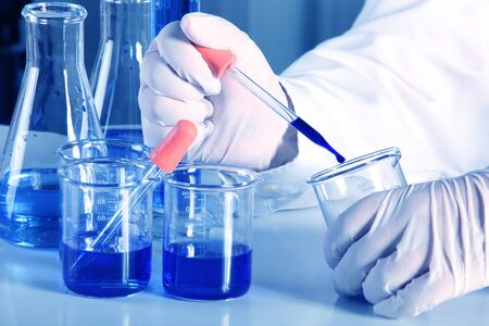 Flask in scientist hand with dropping liquid to test tubeの写真素材