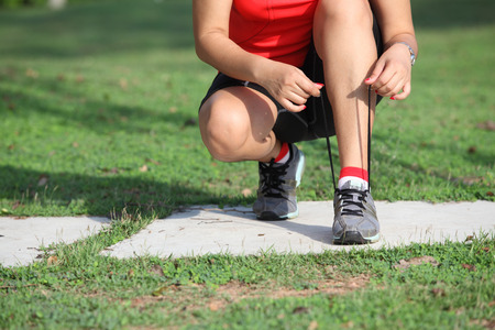 Running shoes - closeup of woman tying shoe laces. Female sport fitness runner getting ready for jogging outdoors on forest path in spring or summer.の写真素材