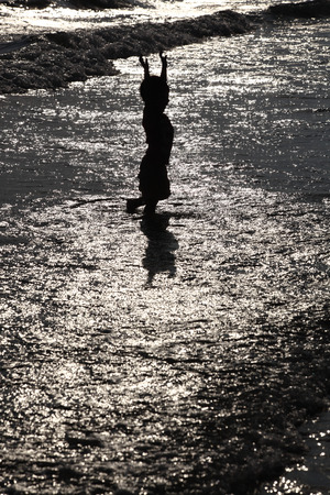 Silhouette of child on the beach, holding his hands up, hugging the sunの写真素材