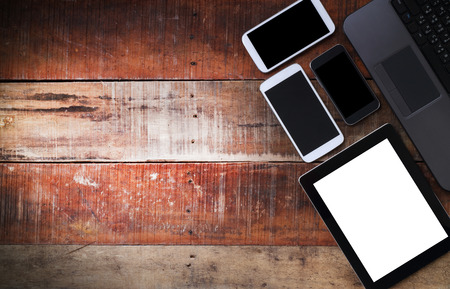 Open laptop with digital tablet and white smartphone. All with isolated screen on old wooden desk.の写真素材