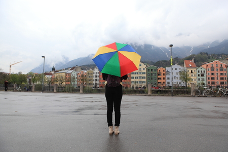 multicolor umbrella yellow woman against the rain at innsbruck, austria - historic architecture, snow capped mountains, and the inn river in the old alpine town of innsbruck, tyrol, austria.の写真素材