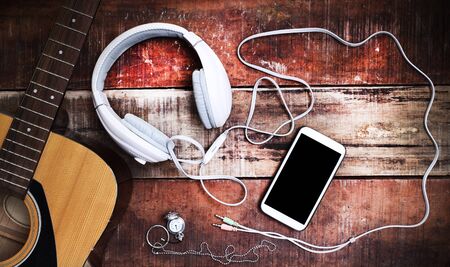 Acoustic guitar ,cell phone and headphone on old wooden tableの写真素材
