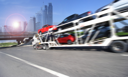 The trailer transports cars on highway with big city background