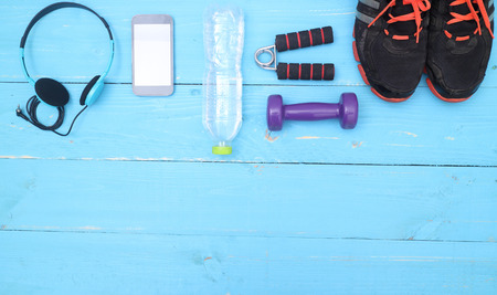 Flat lay shot of Sport equipment. Sneakers, water, earphones and phone on wooden background. Focus...