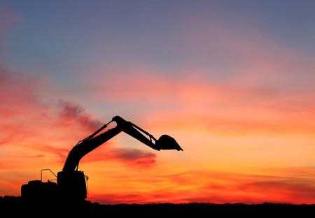 silhouette of Excavator loader at construction site with raised bucket over sunsetの写真素材