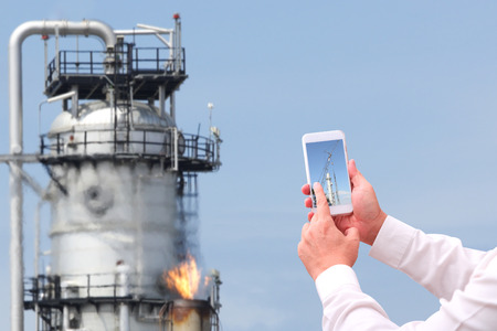 industry 40 concept man hand holding cellphone in smart factory background  against oil refinery...