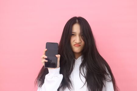 happy excited  glad to receive text message informing about salary, rejoices good news, stares at mobile phone, actively from happiness, Beautiful Asian models over  pink  background for advertising conceptの写真素材