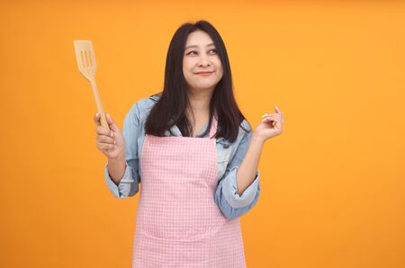 Happy Asian woman is cooking with apron for cooking advertise theme on on yellow background.の写真素材