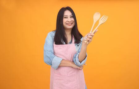 Happy Asian woman is cooking with apron for cooking advertise theme on on yellow background.の写真素材