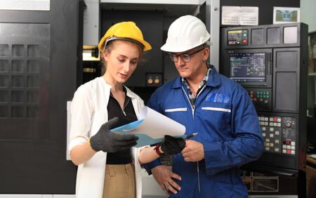 Male and Female Industrial Engineers in Hard Hats Discuss New Project while Using Laptop. They Work in a Heavy Industry Manufacturing Factory.の写真素材