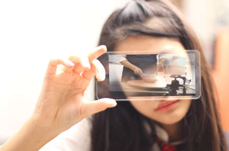 Online study concept,  individual self- student using mobile phone for e-learning, distance learning, rear view over shoulder, focus on screen for food channel.の写真素材
