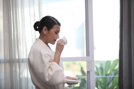 Portrait of smiling happy cheerful beautiful pretty asian woman relaxing drinking and felling enjoy having breakfast in holiday morning vacation on bed at homeの写真素材
