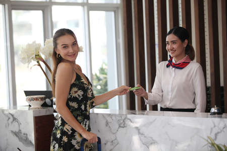 Happy young woman at hotel reception receiving the key of the room.  or good receive get take care from service from hotelの写真素材