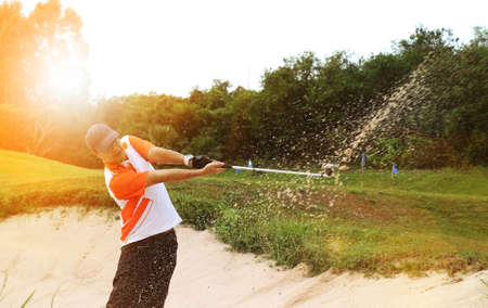 man playing golf on a sunny day moving sand in the banker