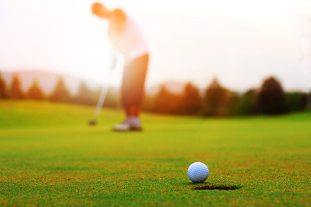 Golfing game. Asian man golfer action to win after winner long putting golf ball on the green golf, outdoors sunset time , Pro golfer putting golf ball in to the hole.の写真素材