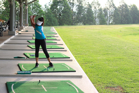 Woman golf player swing shot on course or Girl golf player with driver shoot over lake, view from behind.の写真素材