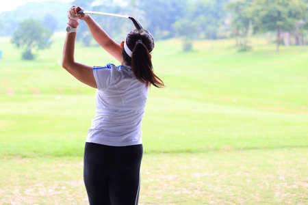 Woman golf player swing shot on course or Girl golf player with driver shoot over lake, view from behind.の写真素材