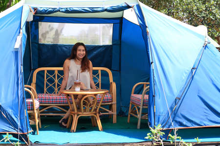 Beautiful young woman in tent camping just on sand of the beach. Girl smiling in tent. Happy traveler people enjoying the alternative vacation  with tent and beautiful young woman  looking forestの写真素材