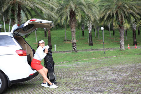 woman travel by car to golf, woman loading a golf bag into the boot of a parked car on the driveway.の写真素材