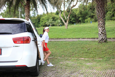 woman travel by car to golf, woman loading a golf bag into the boot of a parked car on the driveway.の写真素材