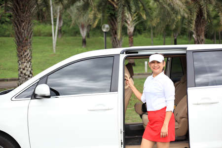 woman travel by car to golf, woman loading a golf bag into the boot of a parked car on the driveway.の写真素材