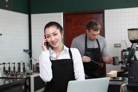 Portrait of a handsome barista and girl in apron at the bar of the modern cafe cheerful men baristas wearing aprons working at the counter in cafe indoors, talking , owned business , new lifeの写真素材