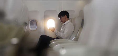 Young asian businessman  sitting in business first class seat inside airplane via using smartphone with happinessの写真素材