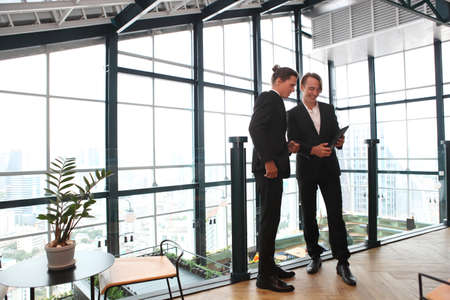 two young business people working and communicating while standing at the office with city building background.の写真素材