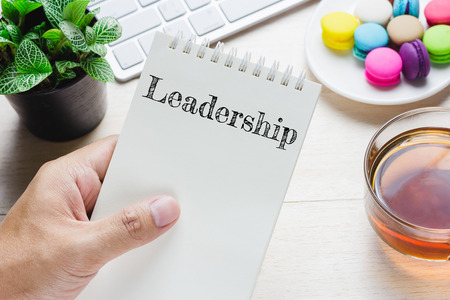 Man holding Leadership message on book and keyboard with a hot cup of tea, macaroon on the table. Can be attributed to your ad.の写真素材