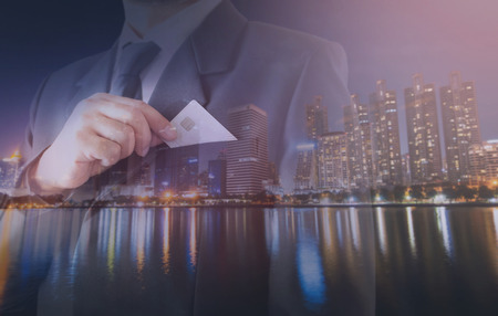 Double exposure of city and businessman standing Holding a credit card.の写真素材