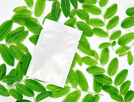 White cream bag on blank label package for mock up on a green leaves background. The concept of...