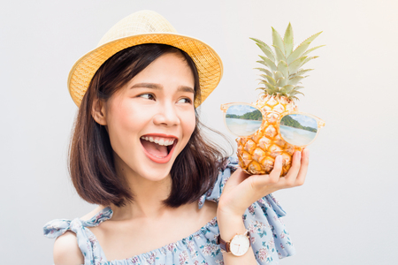 Young girl happy smile and cheerful in blue dress and hold pineapple in hand, Wear sunglasses with a reflection of the beach and island. Concept summer travel.の写真素材