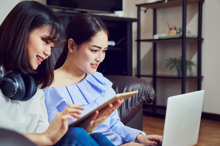Asian girl in blue casual dress listening to music from black headphones and use laptop. In a comfortable and good mood, In the living room on the sofa.の写真素材