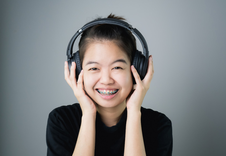 Asian girl in black casual dress listening to music from black headphones. In a comfortable and good mood, on a gray background gives a soft light.の写真素材